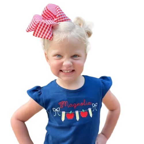 Child wearing a blue shirt with 'Magnolia' and apple design, standing outdoors.