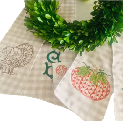 Decorative tablecloth with printed designs of a turkey, pumpkin, and wreath on a white background.