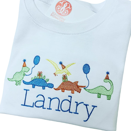 White shirt with embroidered dinosaurs and the name 'Landry' on a white background