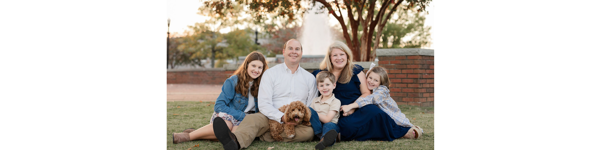 Family of five sitting on grass with a dog in a park